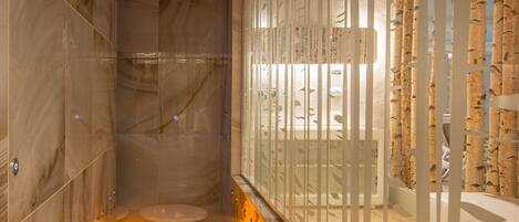 A modern bathroom with marble walls, a glass partition, and a bathtub.
