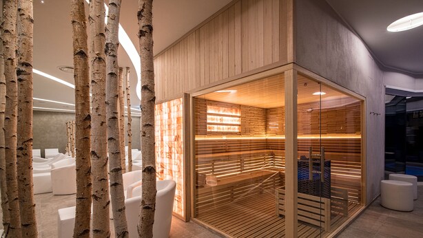 A modern spa area with birch trees, white seating, and a wooden sauna.