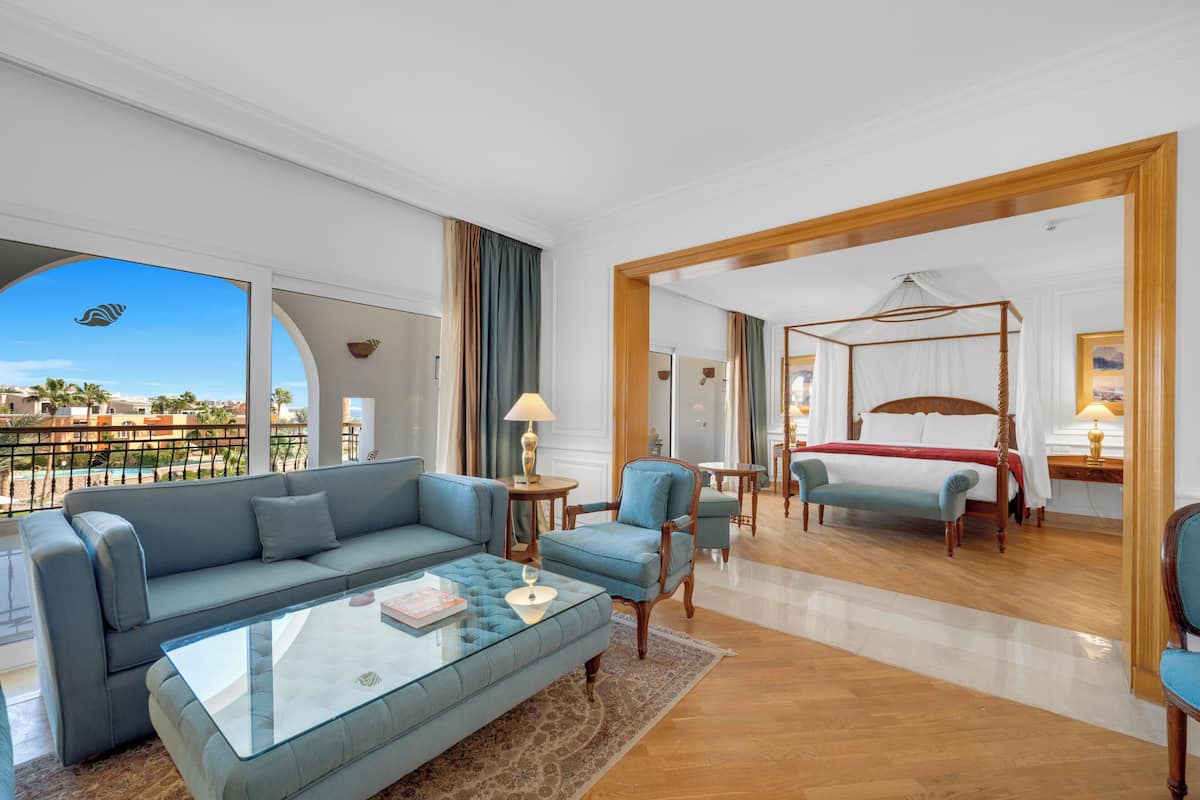 A hotel room with a sofa, armchair, glass coffee table, and a four-poster bed.