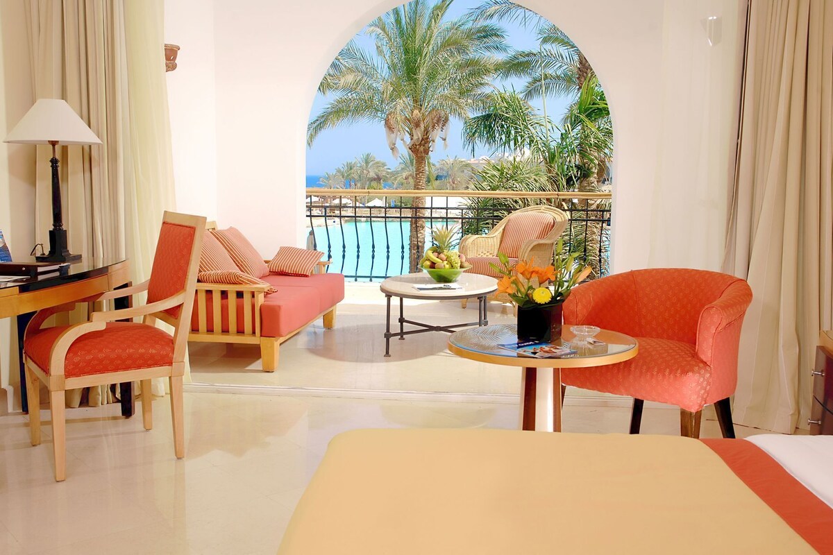 A hotel room with a balcony, a sofa, a chair, a small table, and a bed.