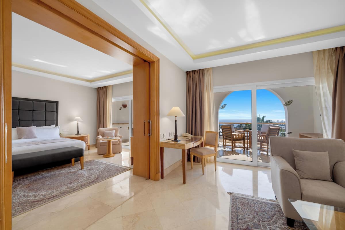 A hotel room with a bed, desk, chairs, a balcony with a view, and a sofa.