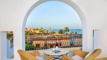 A balcony with wicker chairs, a small table, and a view of the sea and buildings.