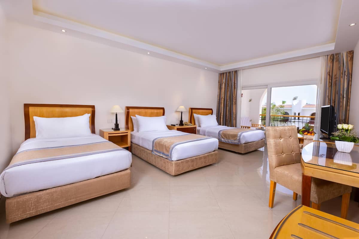 A hotel room with three beds, a dining table, and a TV.