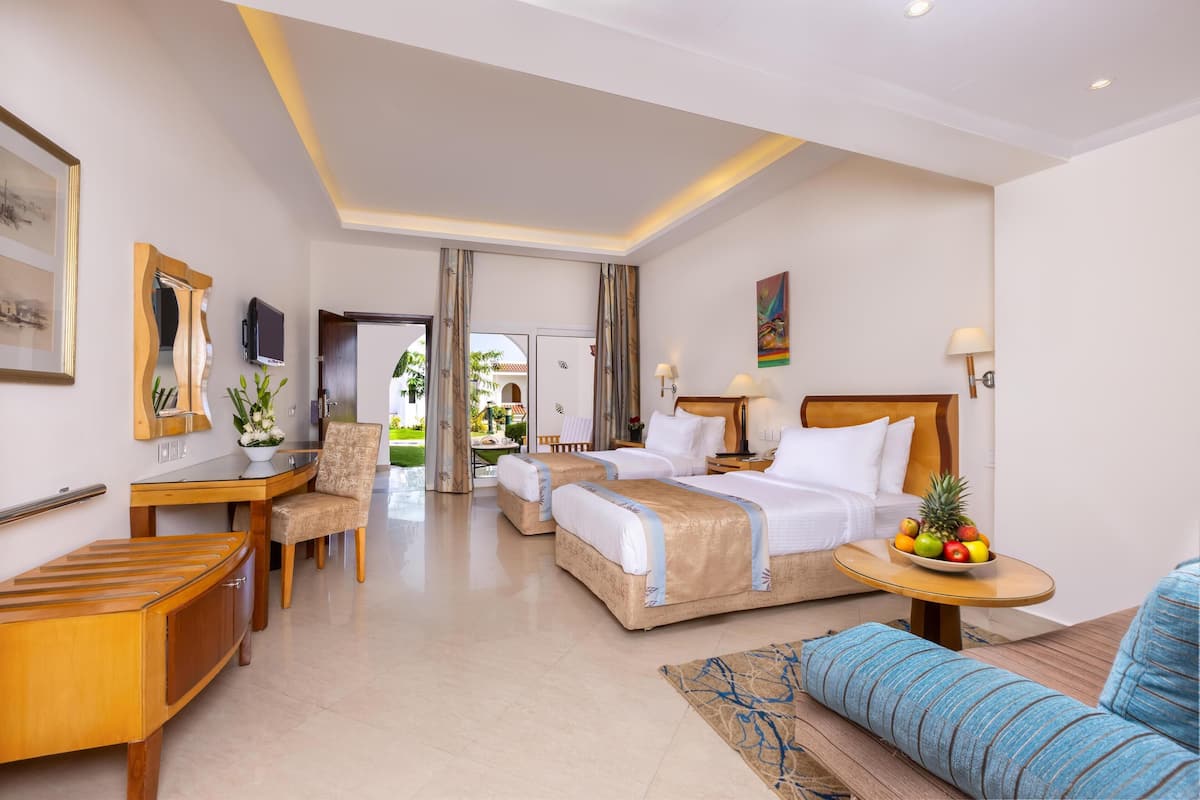 A hotel room with two beds, a desk, a chair, a sofa, and a small table with fruit.