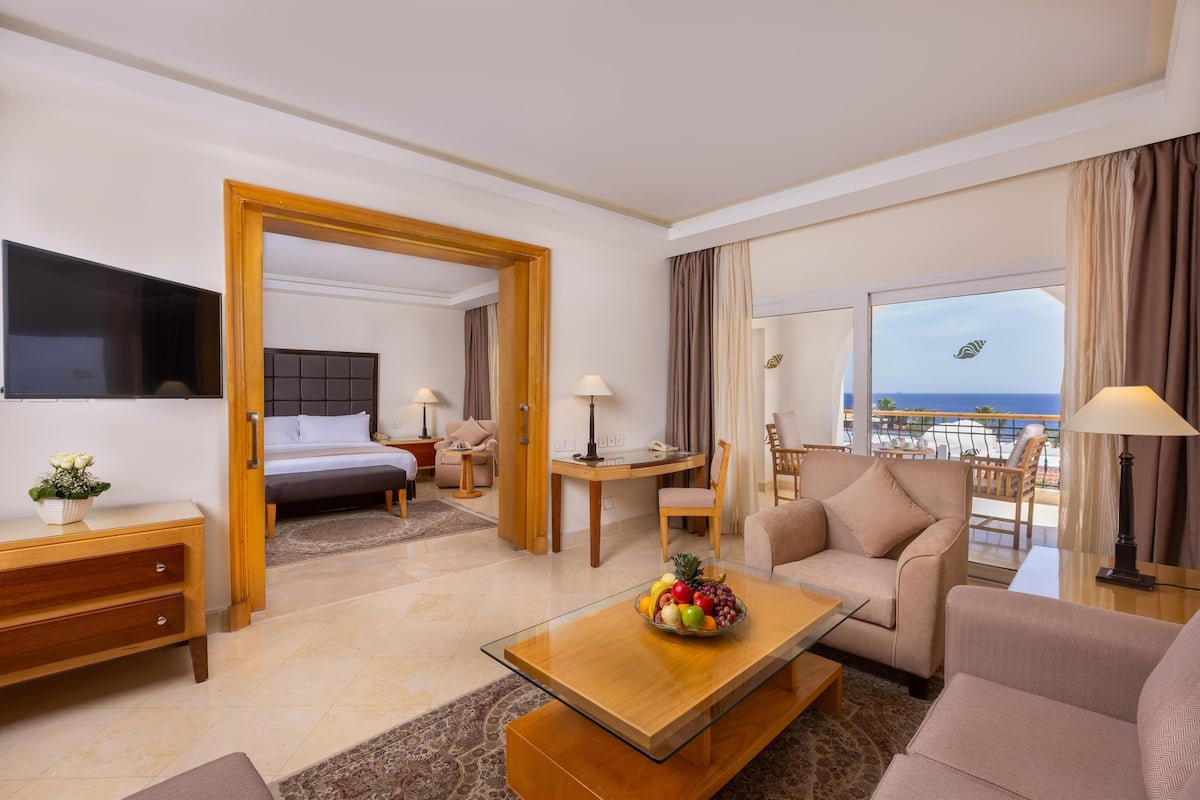 A hotel room with a bed, a desk, a sofa, a TV, and a balcony with a view of the sea.