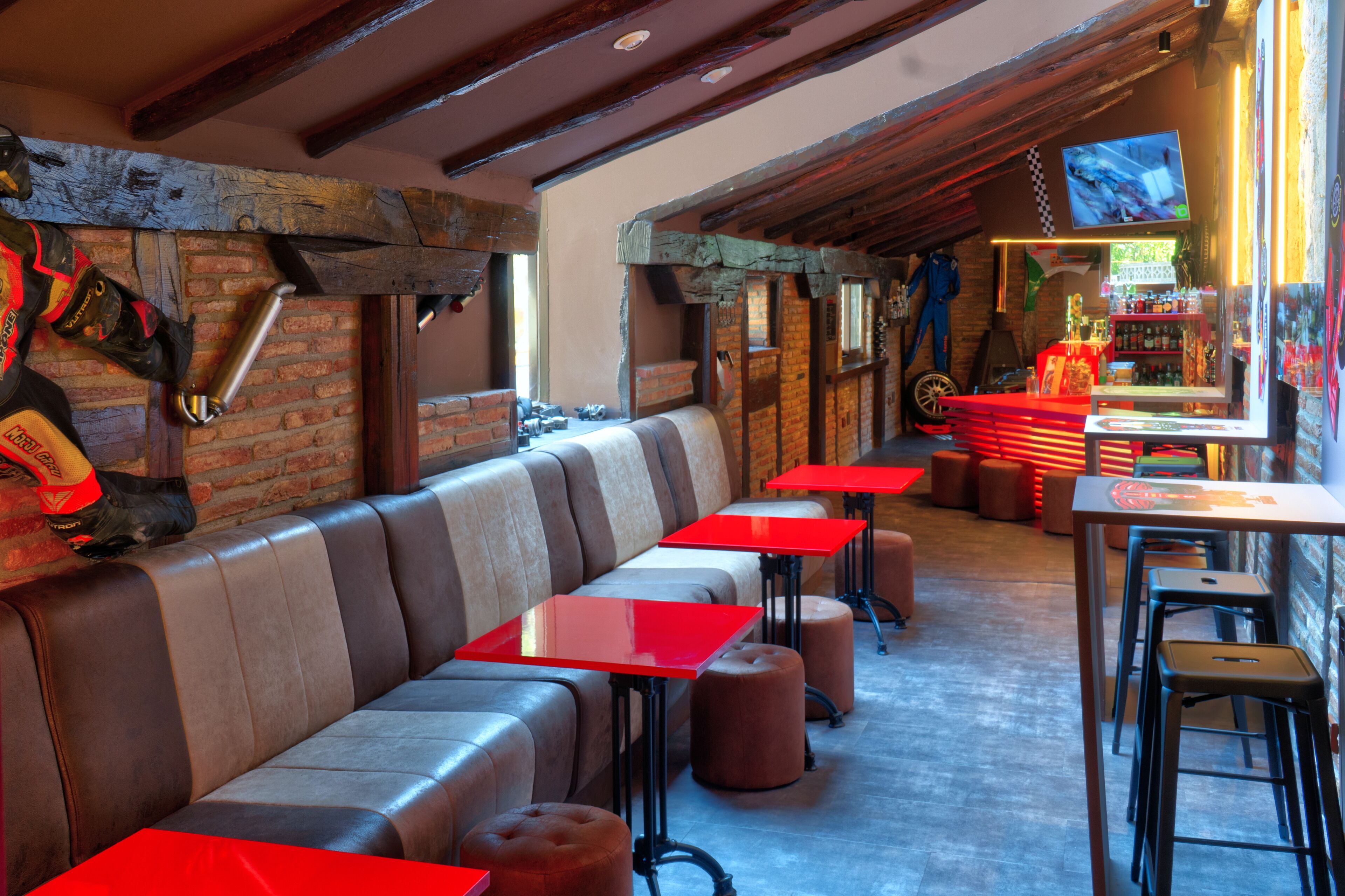 A restaurant with a long bench seating area, red tables, and stools.