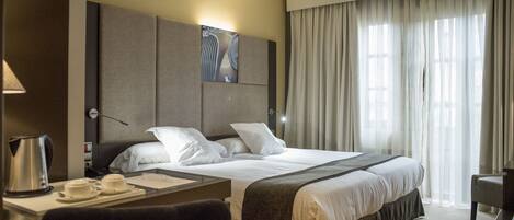 A hotel room with a large bed, a desk with a lamp, a chair, and a painting on the wall.