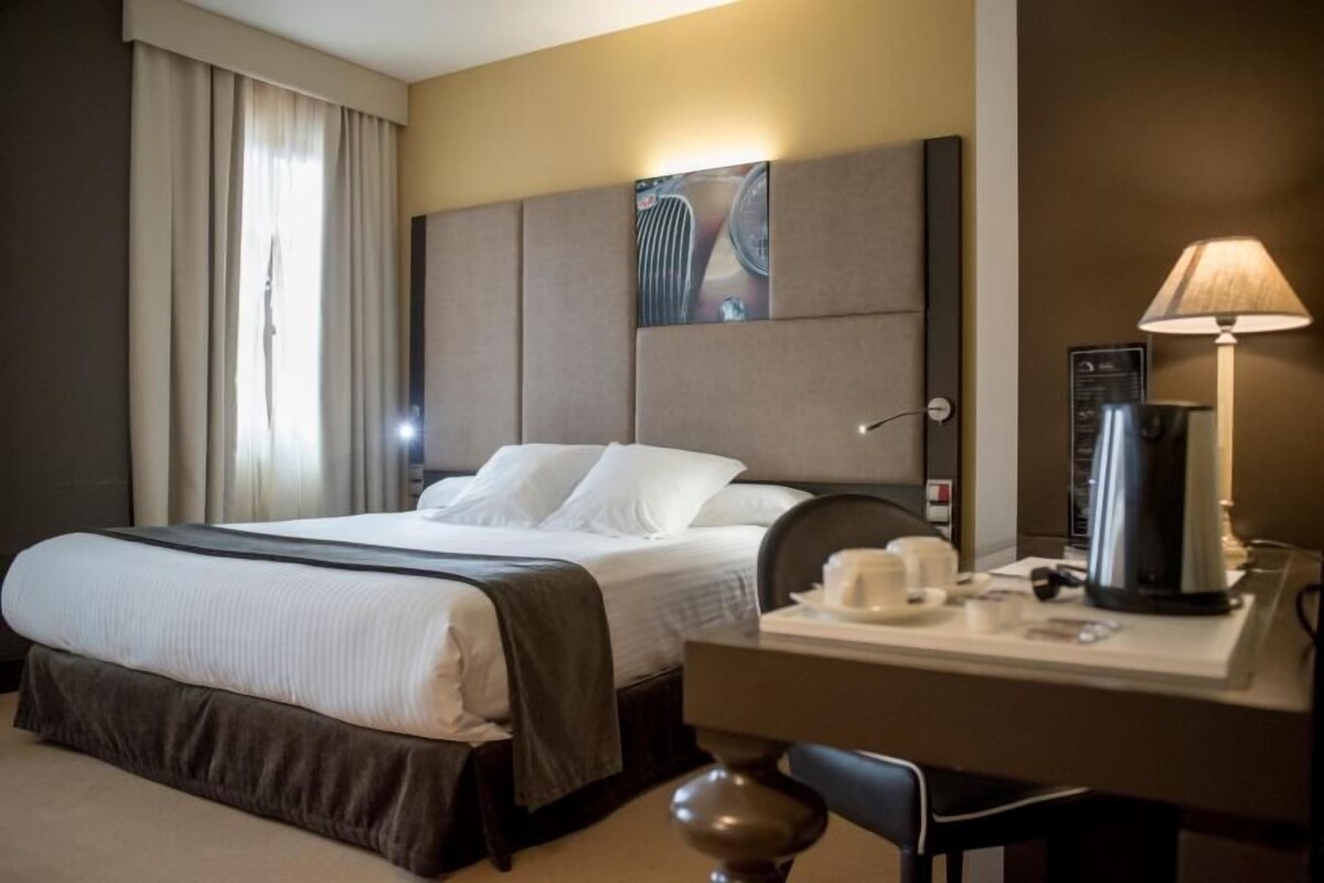 Una habitación de hotel con una cama, un escritorio con lámpara y una cafetera.