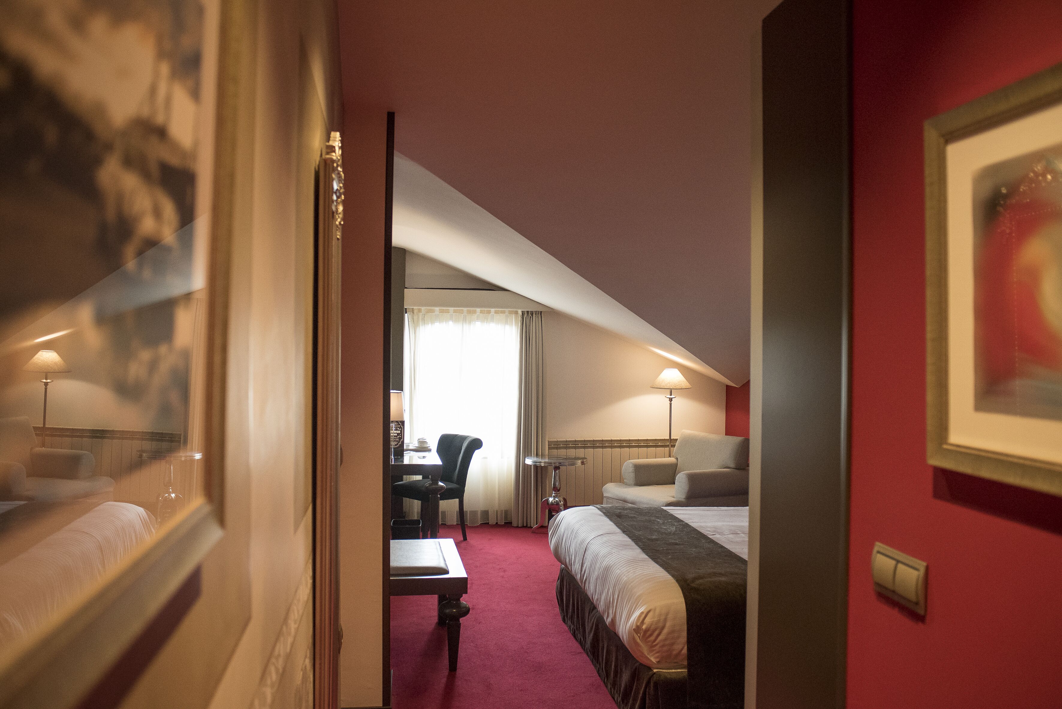 A hotel room with a bed, a desk, a chair, and a lamp.