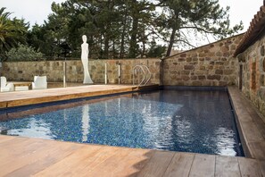 A swimming pool with a stone wall and wooden deck. - Costa Esmeralda Suites (Suances)