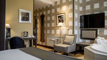 A hotel room with a bed, a chair, a desk with a lamp, a television, and a bathroom with a bathtub.