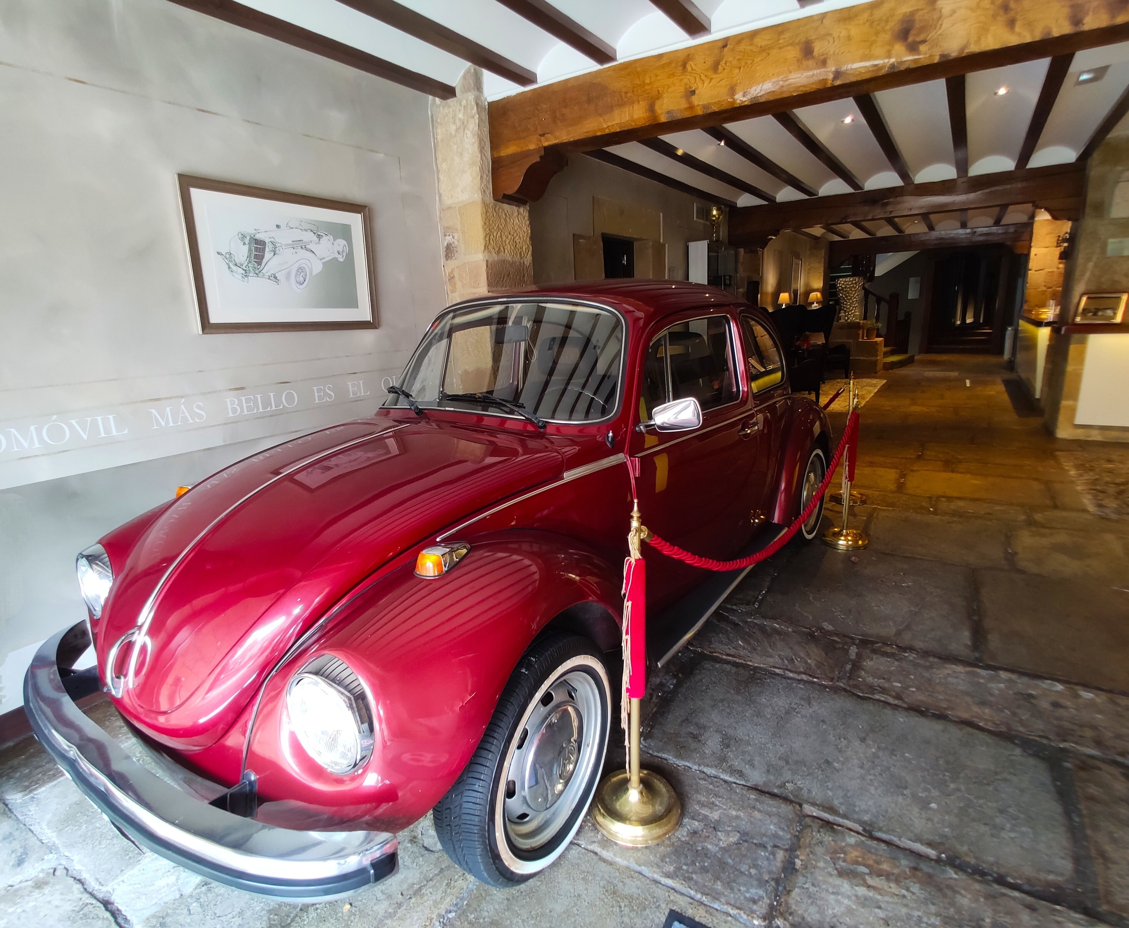 Un coche rojo antiguo estacionado en el interior, rodeado de muros de piedra y vigas de madera.