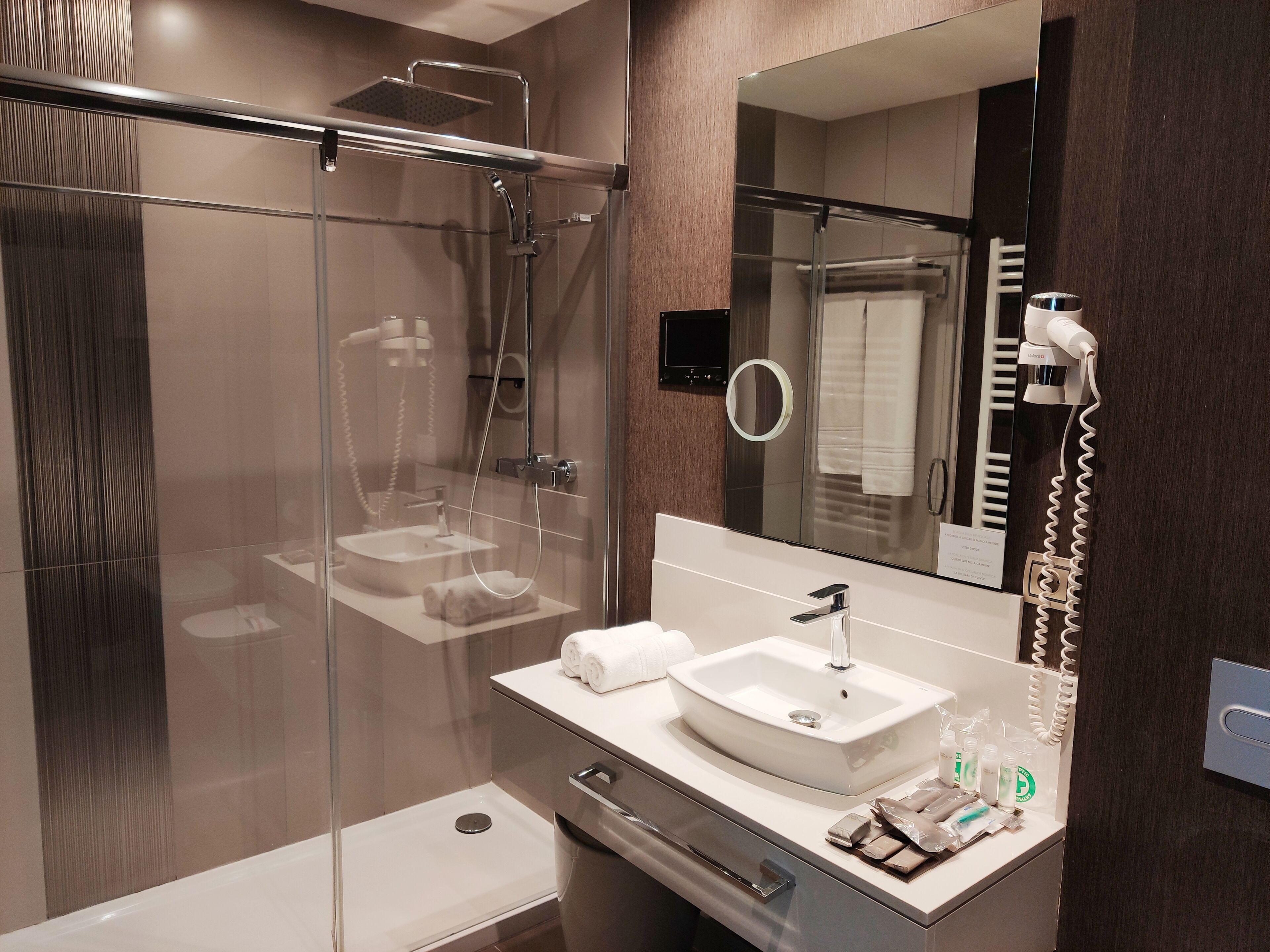 Un baño moderno con ducha de vidrio, un lavabo con espejo y artículos de aseo en la encimera.