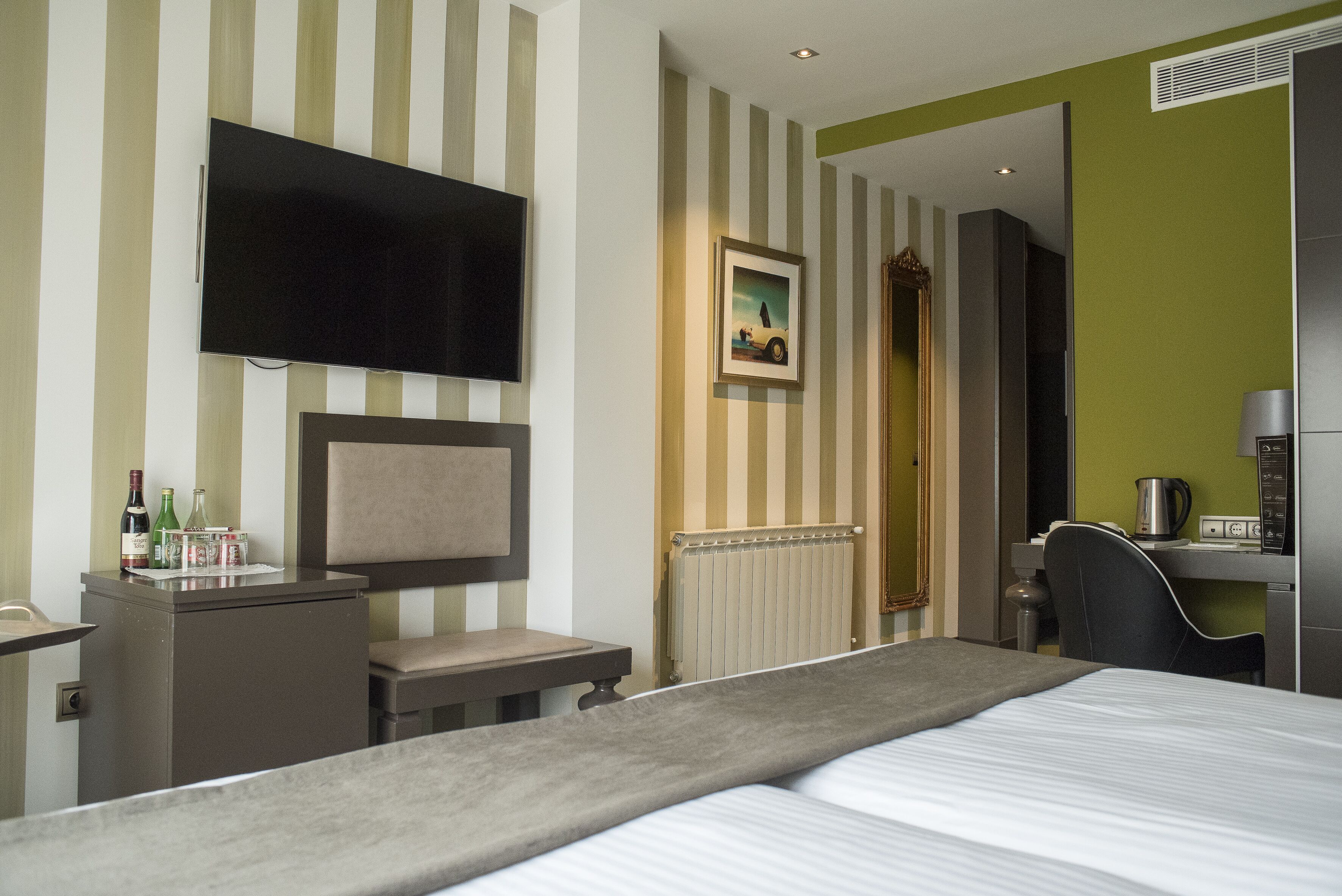 Ein Hotelzimmer mit Bett, Schreibtisch, Sessel, Fernseher und Heizkörper.