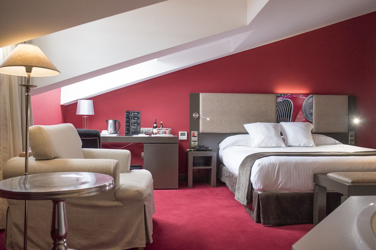 A hotel room with a bed, a desk, a chair, and a lamp.