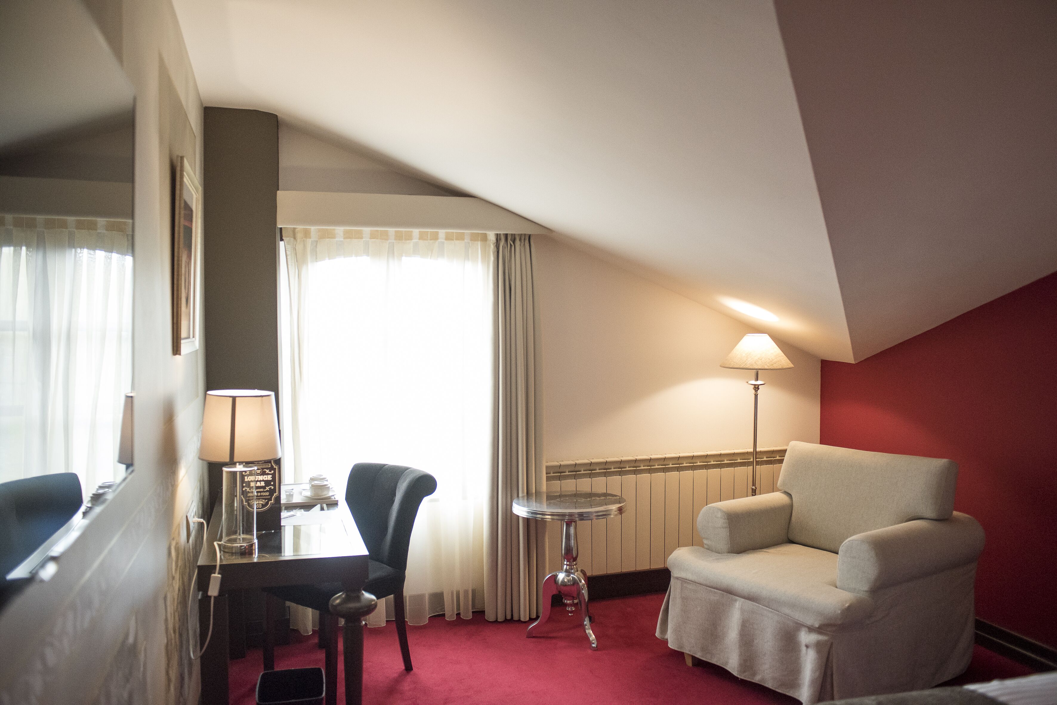 Habitación de hotel con una mesa de comedor, dos sillas, una lámpara y una pared de acento roja.