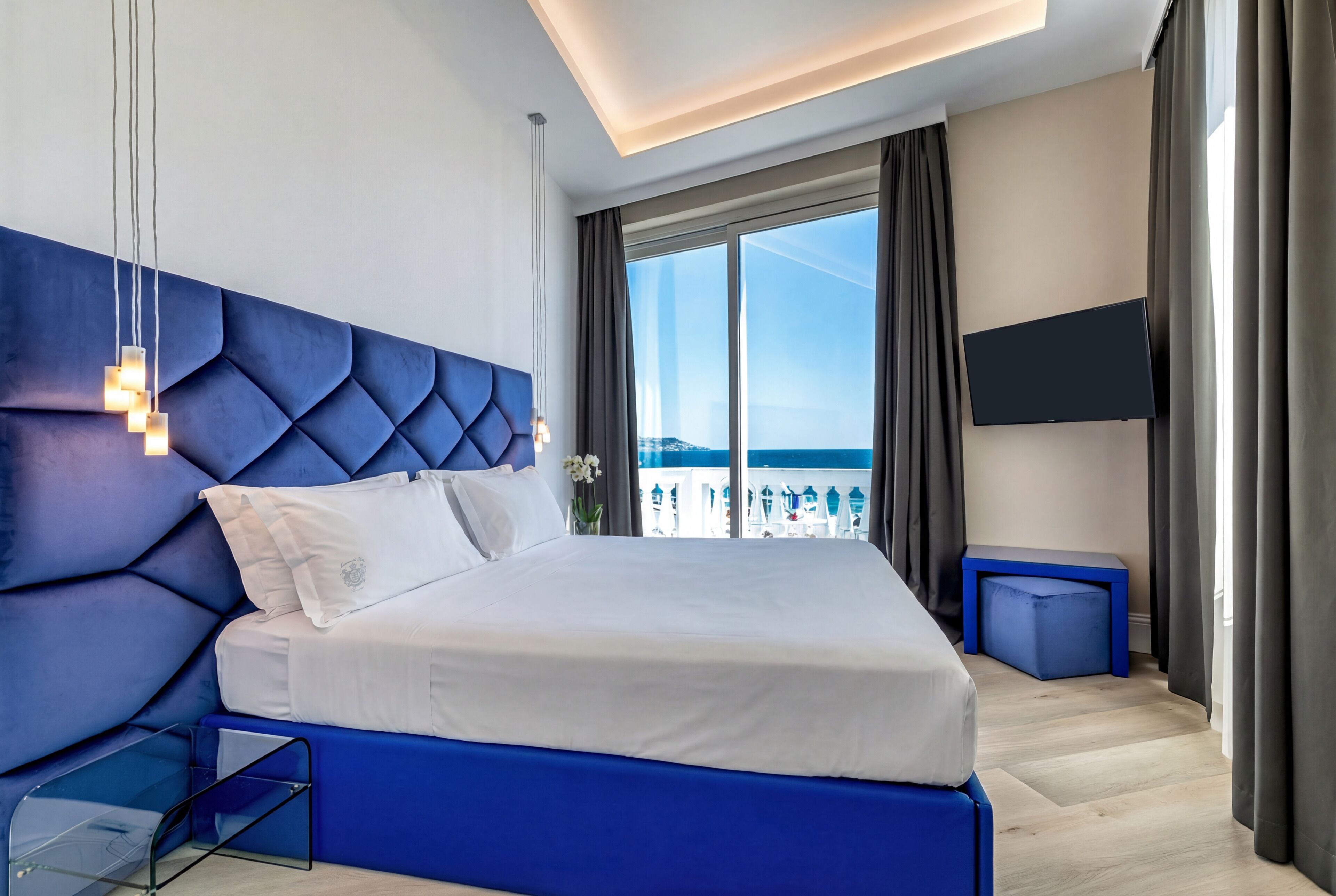 A modern hotel room with a large bed, a TV, and a view of the sea.