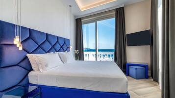A modern hotel room with a large bed, a TV, and a view of the sea.