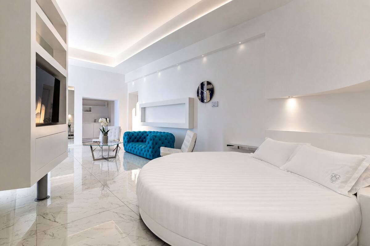 Une chambre d’hôtel moderne avec un grand lit, un canapé bleu, une télévision et une horloge au mur.