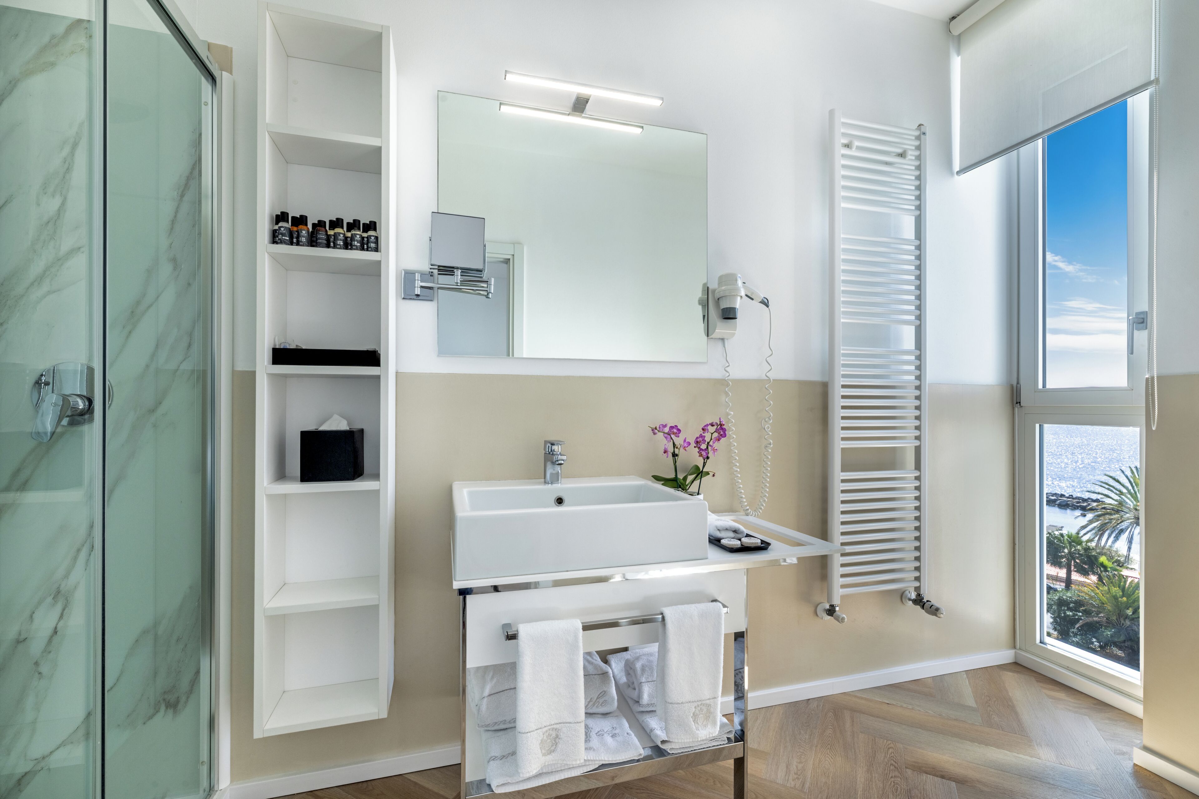 A modern bathroom with a glass shower enclosure, a white sink with a mirror above, and a towel rack with towels.