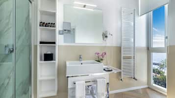 A modern bathroom with a glass shower enclosure, a white sink with a mirror above, and a towel rack with towels.
