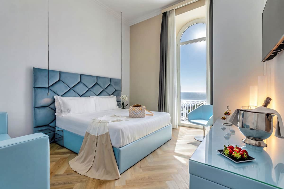 Une chambre d’hôtel moderne avec un lit, une table basse en verre, une vue sur la mer et un balcon.