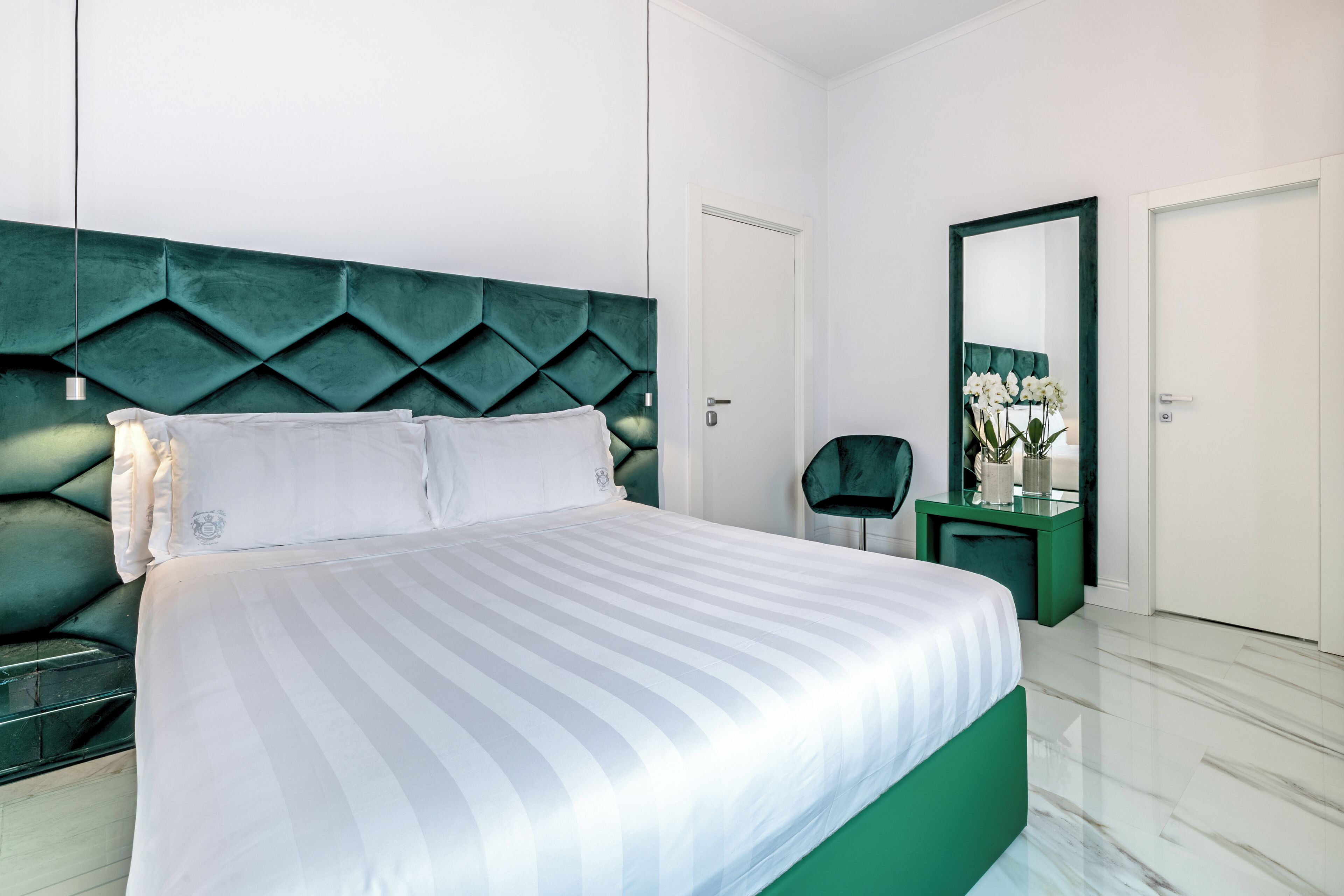 Une chambre moderne avec un grand lit, un mur d’accent vert, une petite table de chevet avec un miroir et une porte.