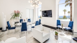 Un salon moderne avec un canapé blanc, des fauteuils bleus, une table à manger et un grand téléviseur.