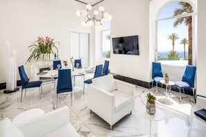 Un salon moderne avec un canapé blanc, des fauteuils bleus, une table à manger et un grand téléviseur.
