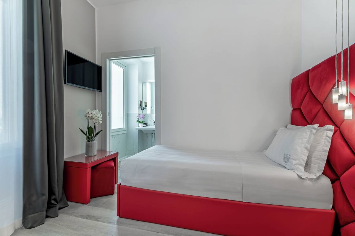 Une chambre à coucher moderne avec un lit rouge, un téléviseur à écran plat et une petite table de chevet agrémentée d’une plante.