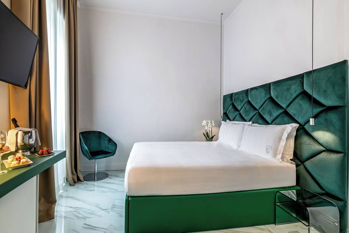 Une chambre d’hôtel avec un lit, un bureau et une chaise, une télévision et une fenêtre avec des rideaux.