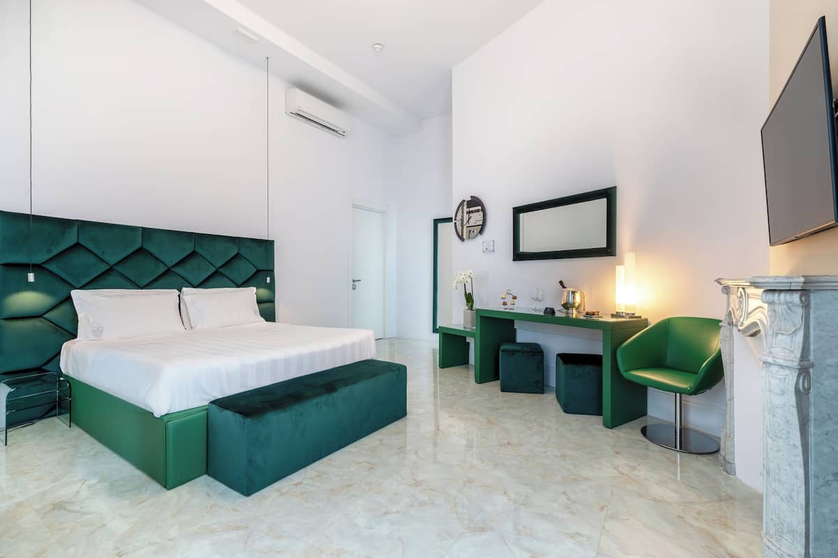Une chambre d’hôtel moderne avec un lit vert, un bureau, une chaise et un sol en marbre.