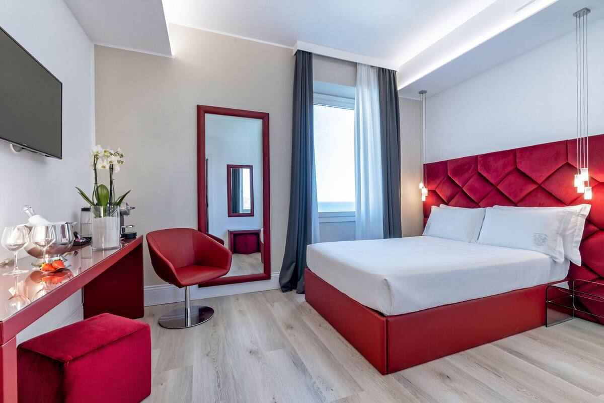 Une chambre d’hôtel moderne équipée d’un lit, d’un bureau avec une chaise, d’une télévision et d’un grand miroir.