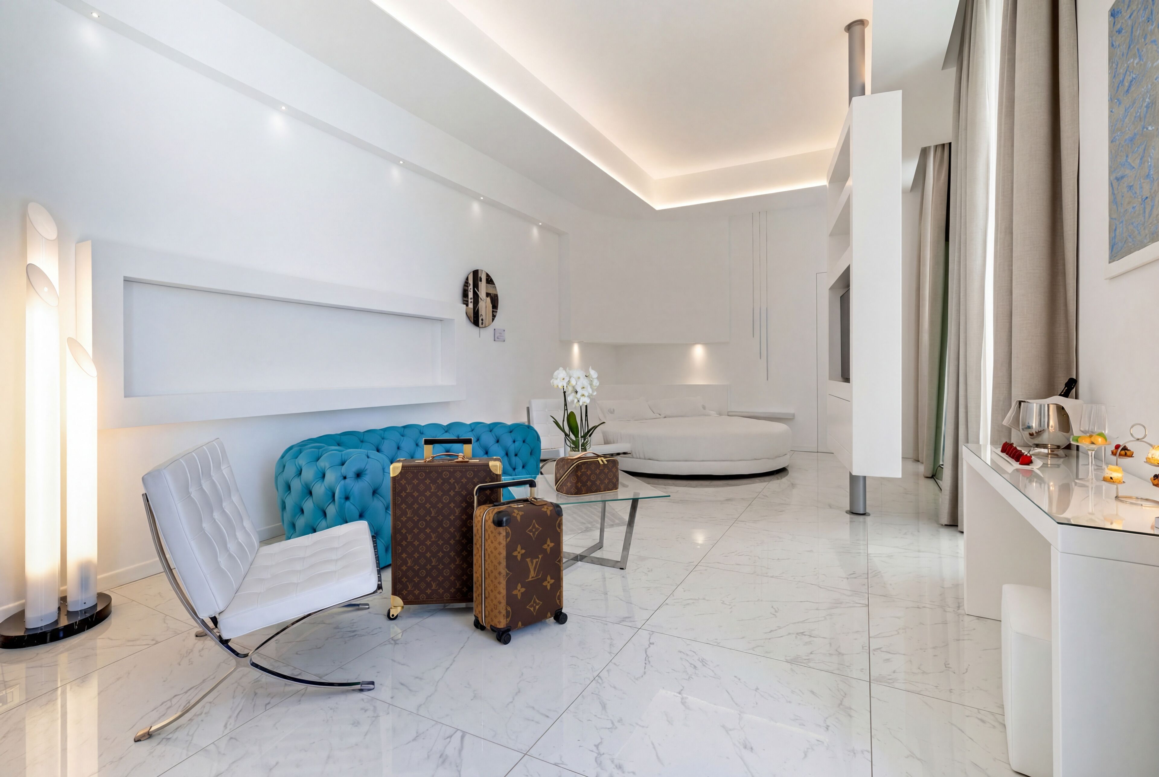 A modern living room with a white sofa, a blue accent chair, and a Louis Vuitton suitcase.