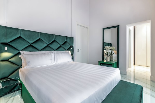 A modern hotel room with a large bed, a green upholstered headboard, a bedside table with a mirror, and a view of the outside.