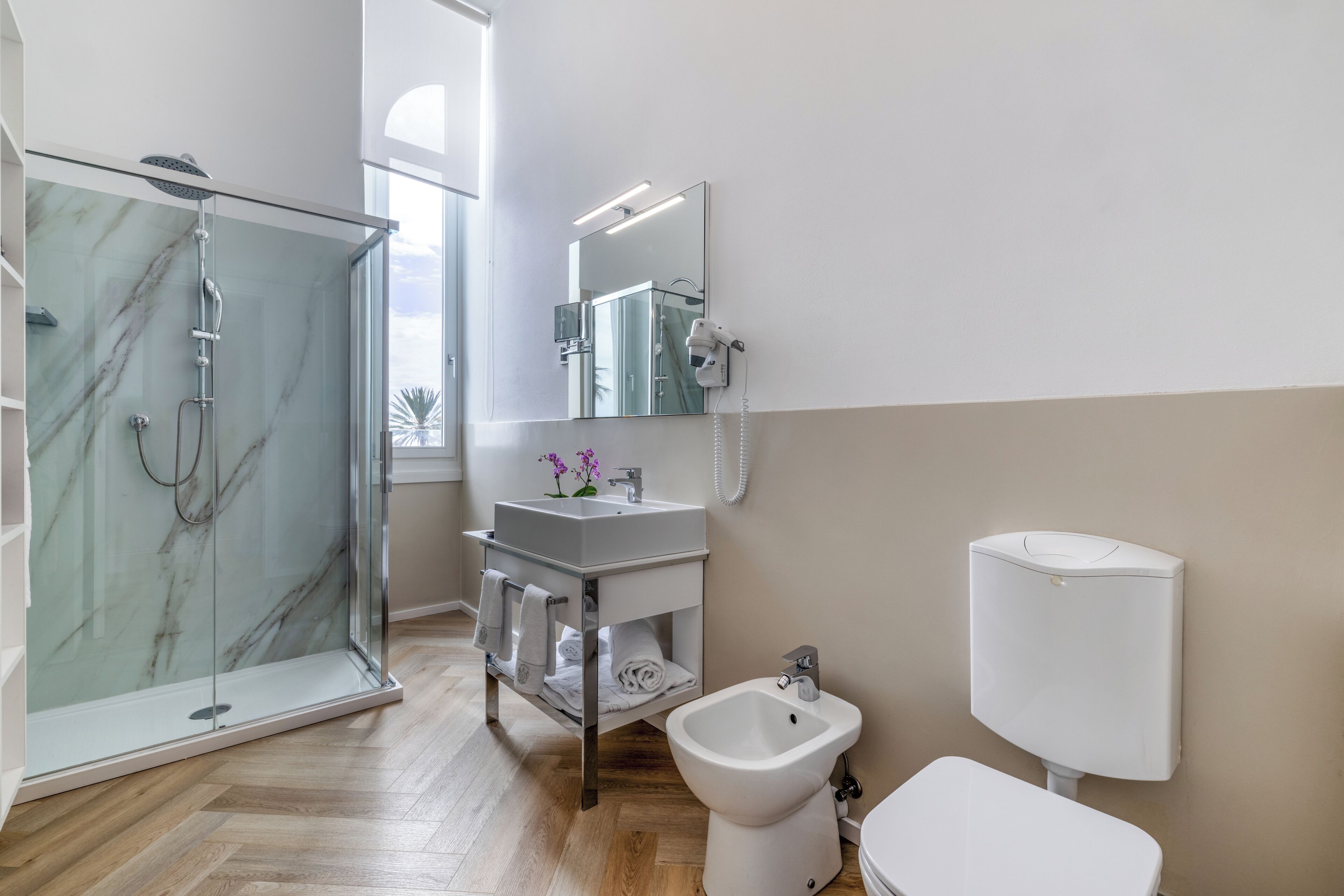 Un baño moderno con ducha de mampara de vidrio, lavamanos blanco, un bidé y un inodoro.