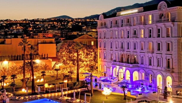 Un hôtel doté d’une piscine, d’un espace extérieur aménagé et offrant une vue sur la ville au crépuscule.