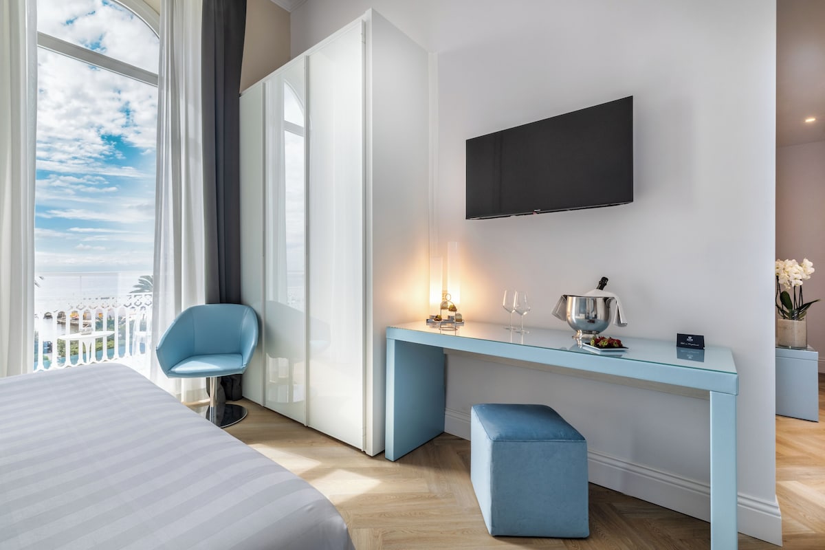Habitación de hotel con cama, escritorio, televisor de pantalla plana, una silla y balcón con vistas.