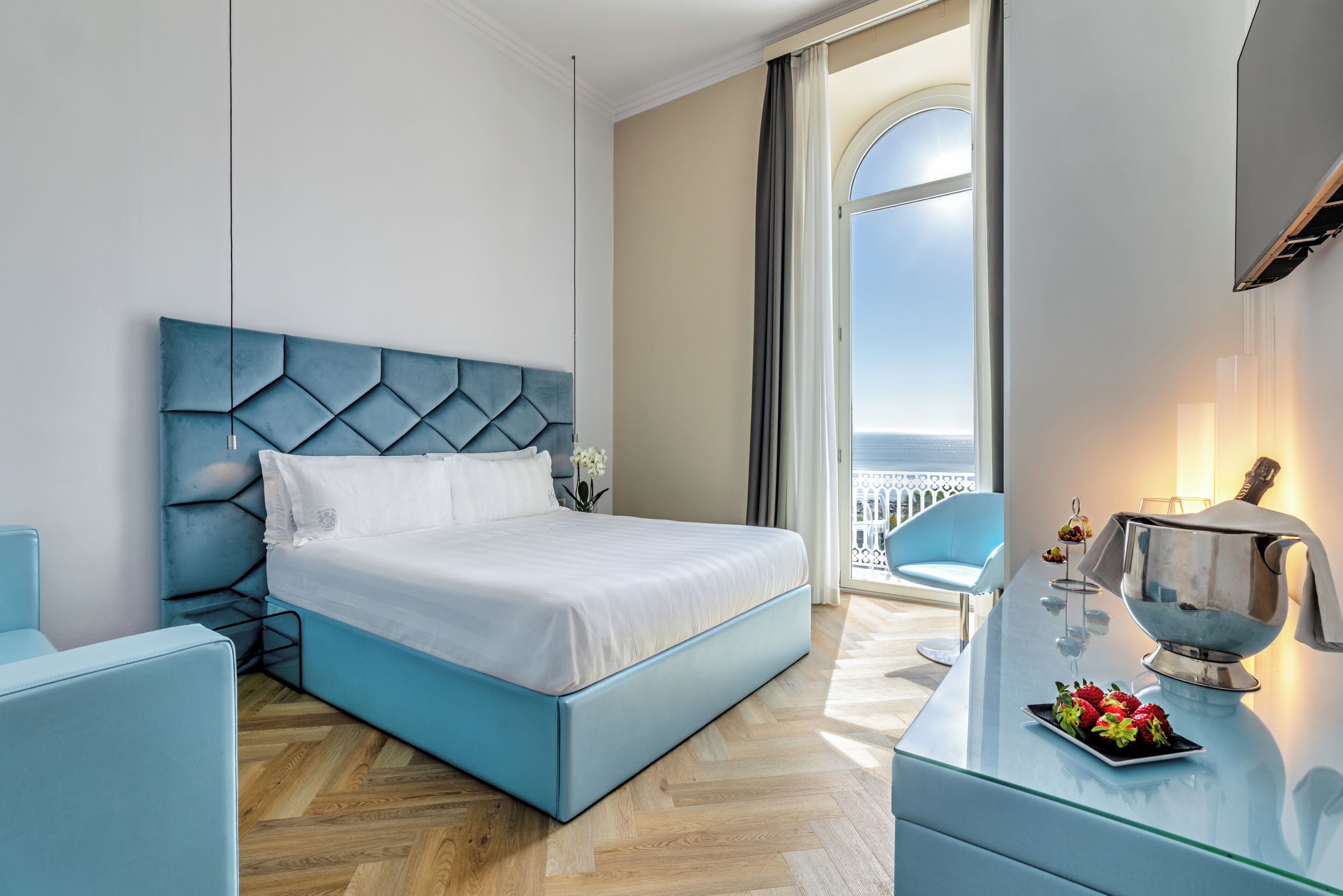A modern hotel room with a bed, a glass coffee table, and a view of the sea.