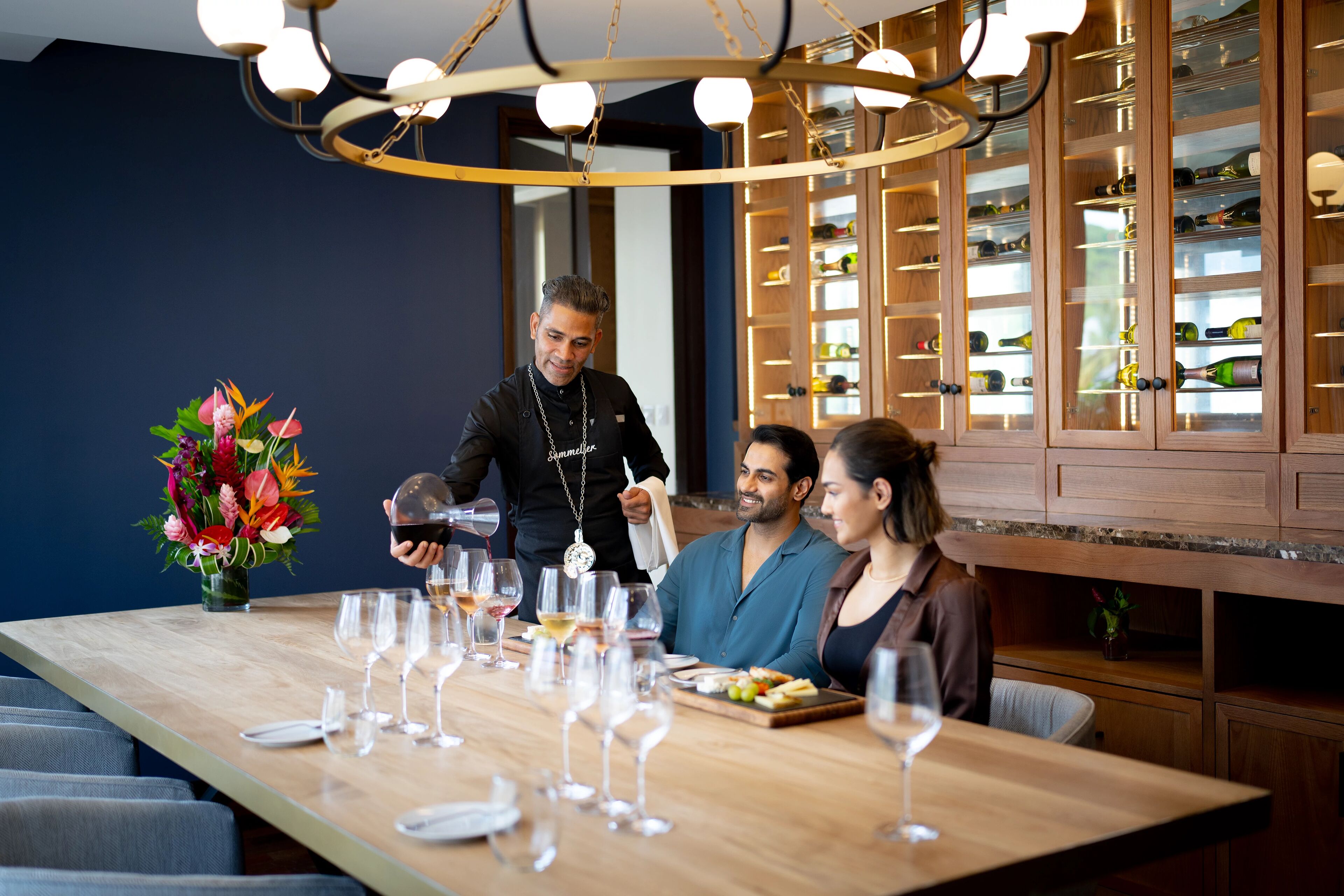 Un comedor con una mesa de madera larga dispuesta para una comida, rodeada de copas de vino y un centro de mesa floral.