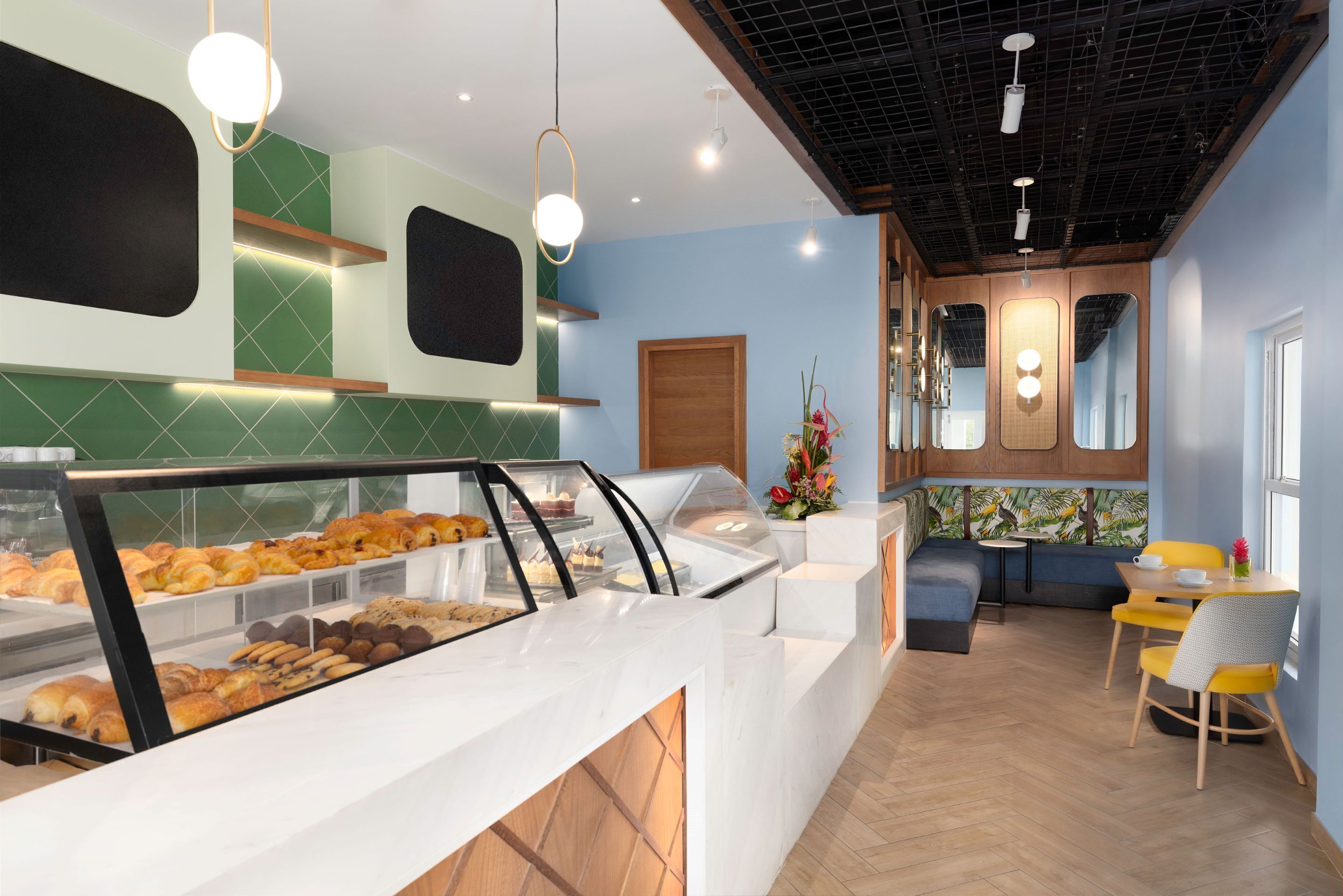 Mostrador de panadería con pasteles, zona de estar con sillas amarillas y techo de madera.