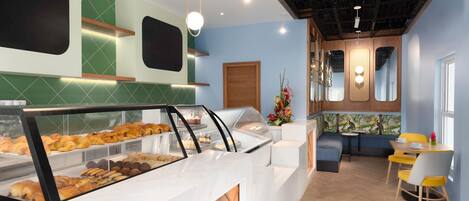 Mostrador de panadería con pasteles, zona de estar con sillas amarillas y techo de madera.