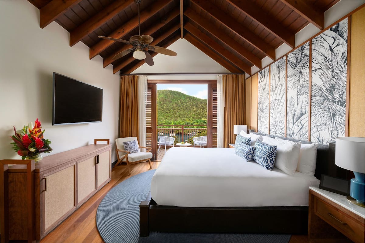 Ein Schlafzimmer mit einem großen Bett, einem Deckenventilator, einem Fernseher, einem Holzschrank, einem Schreibtisch, einem Stuhl und Blick auf einen Balkon mit einem Berg.