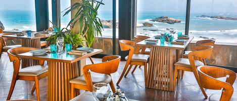 Een restaurant met houten tafels en stoelen, blauwe glazen en uitzicht op de oceaan.