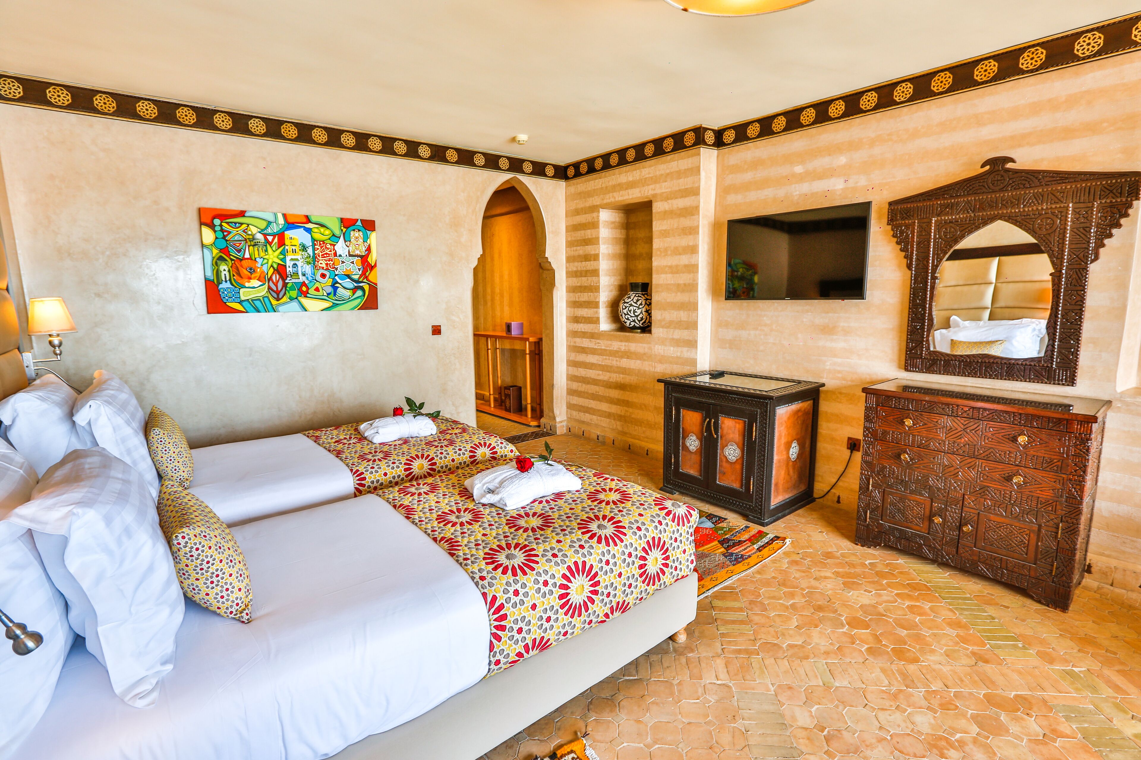 Een hotelkamer met twee bedden, een houten dressoir, een spiegel en een kleurrijk schilderij aan de muur.