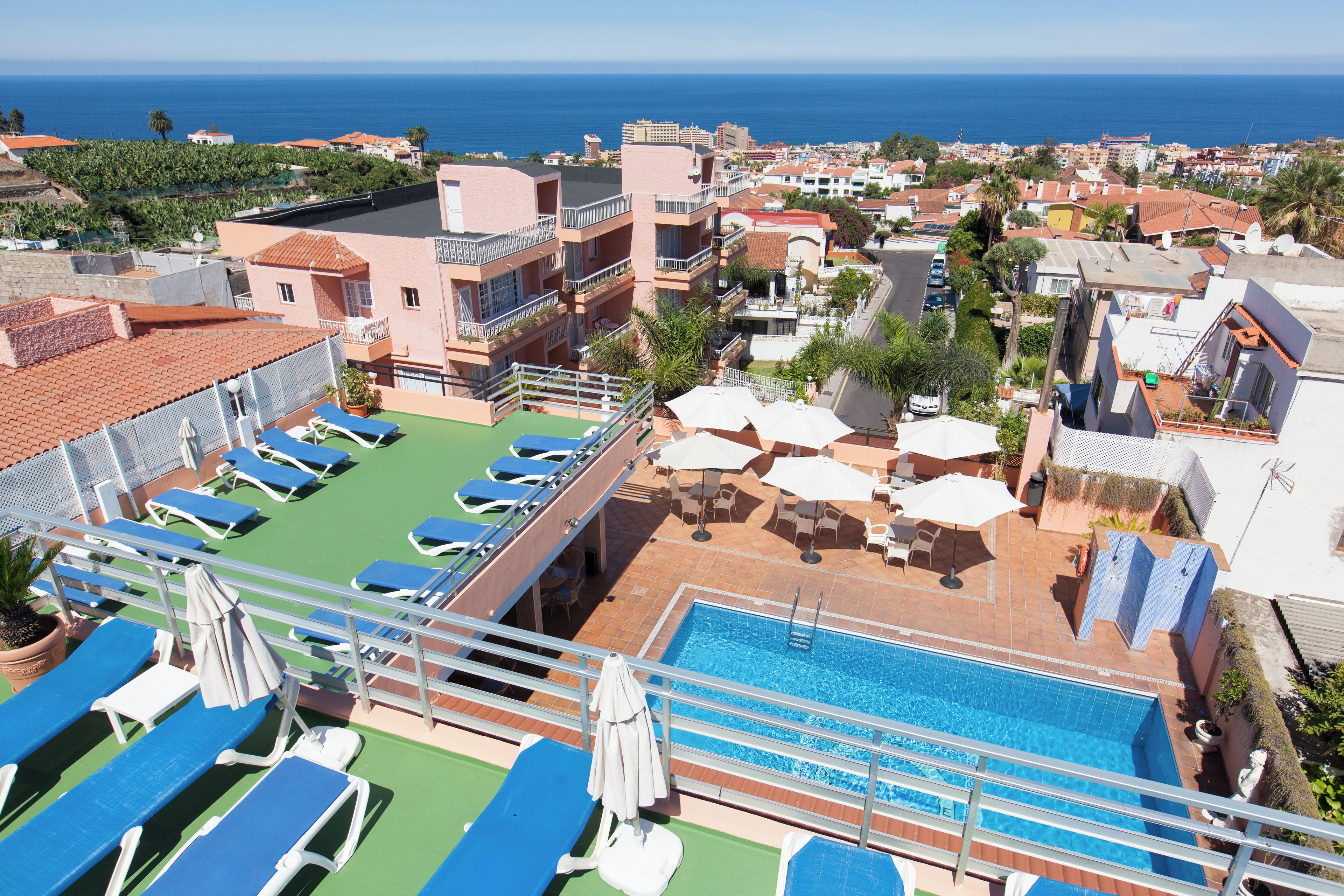A rooftop pool area with lounge chairs and umbrellas, overlooking a coastal cityscape.