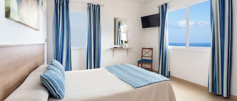 Una habitación de hotel con una cama, una silla, un televisor y un ventanal con cortinas.