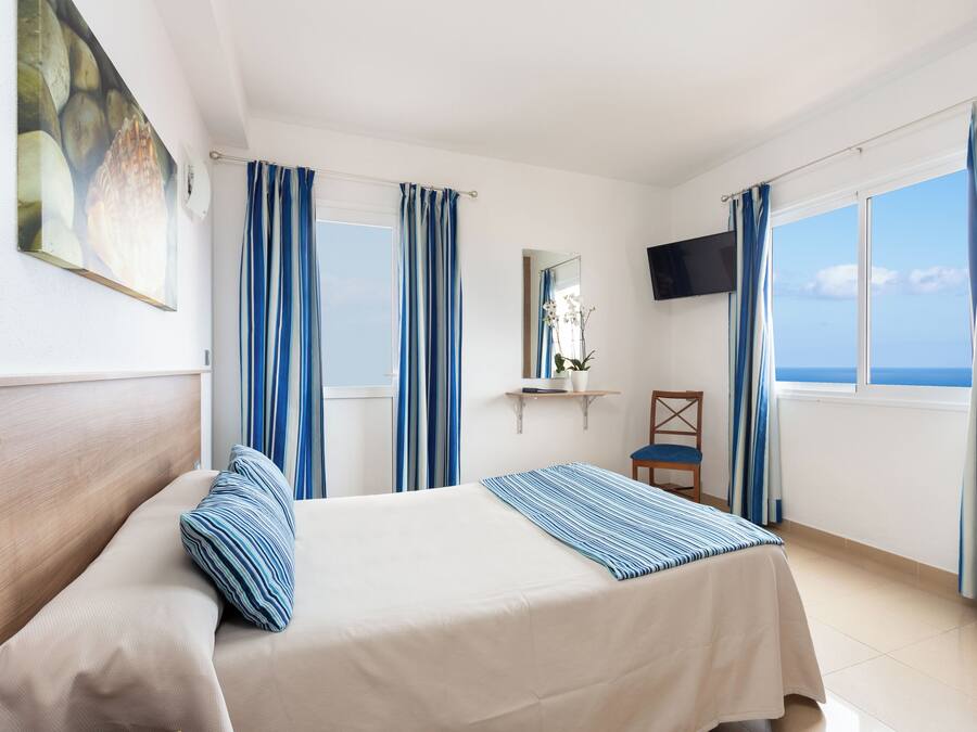 A hotel room with a bed, a chair, a TV, and a window with curtains.
