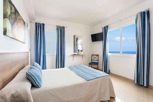 A hotel room with a bed, a chair, a TV, and a window with curtains.