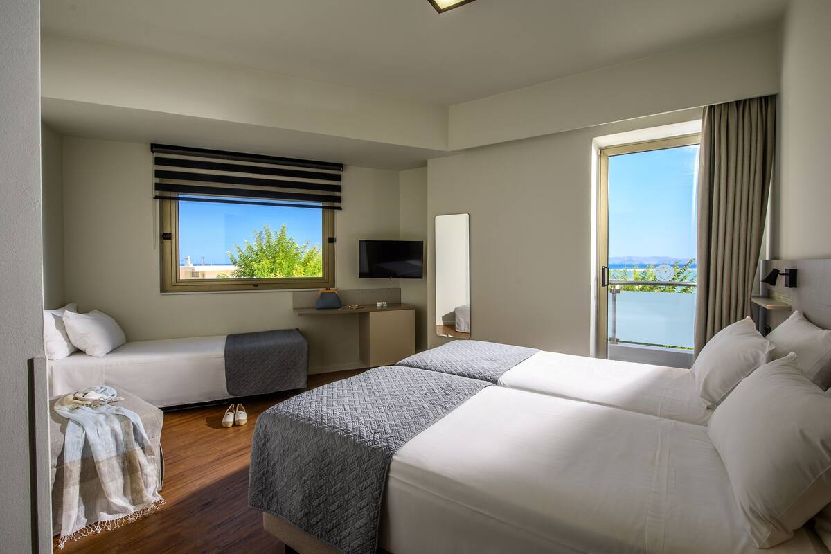 A hotel room with two beds, a TV, a desk, and a large window with a view.